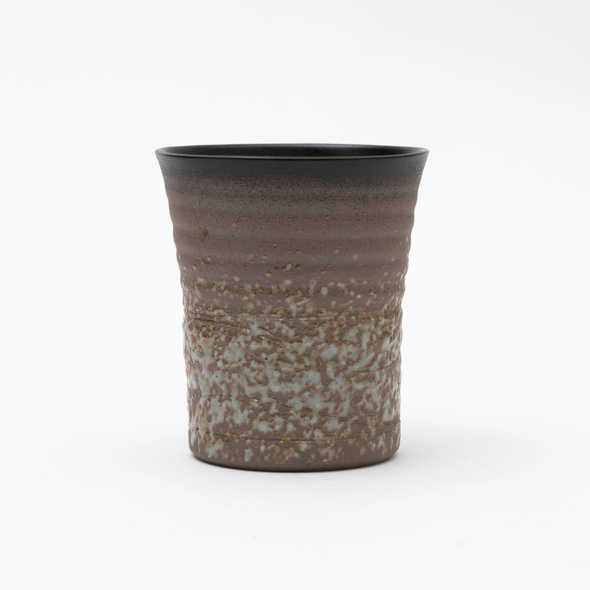 A handleless ceramic tumbler featuring a dark brown ribbed upper section and a heavily textured, speckled grey and brown glaze on the lower half, set against a white background.