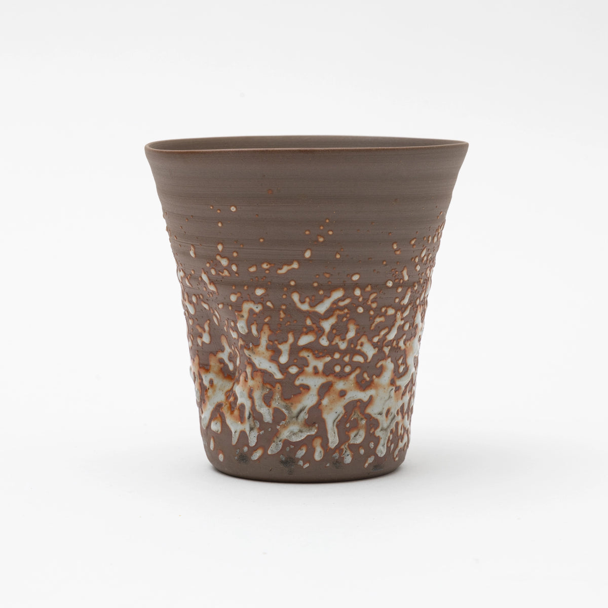 A handleless brown ceramic tumbler featuring a heavily textured, speckled white glaze on the lower half, set against a white background.