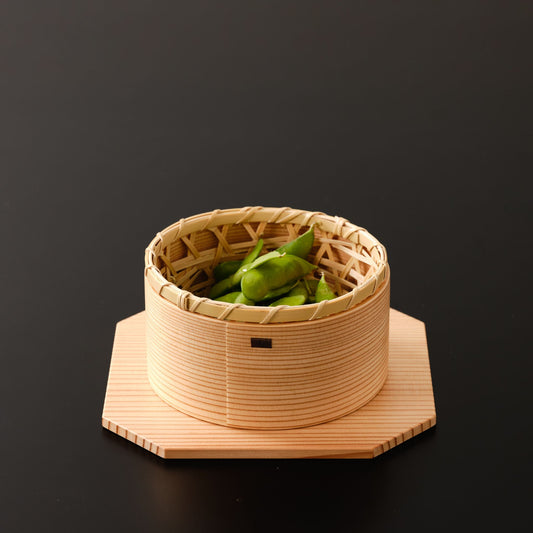 A small bamboo basket with green beans, placed inside a wooden bowl on an octagonal base.