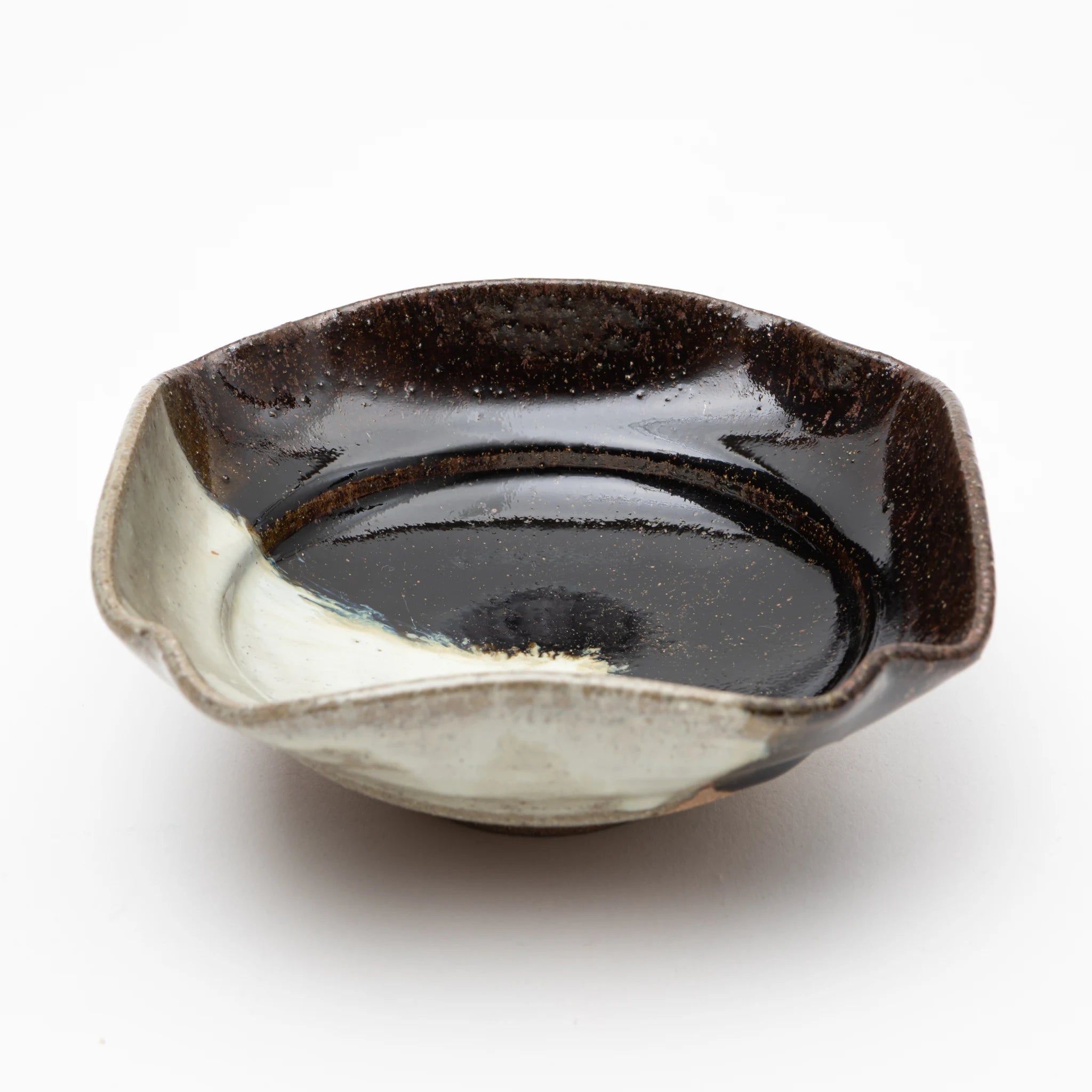 Top-angled view of the Nakazato Tarouemon Chosen Karatsu mukozuke serving dish, showing a squared form with pinched corners, dark iron-black glaze across the upper interior and rim, and milky white ash glaze pooling across the lower interior where the 2 glazes meet.