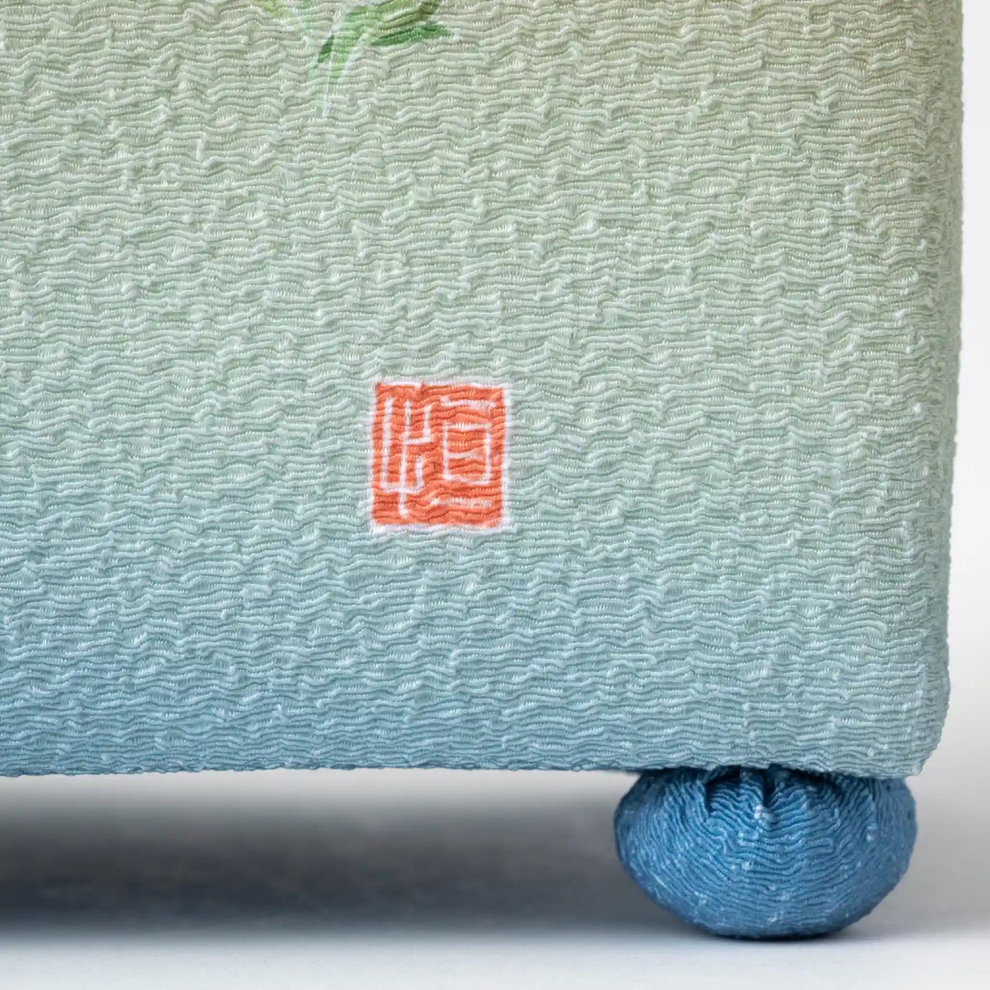 Close-up of the hisatsune YUZEN brand mark on the Kaga Yuzen Autumn Night Accessory Box, showing the intricate texture and soft green shade.