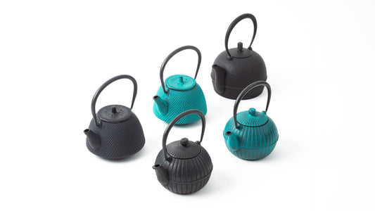 Display of five Nambu Tekki cast iron teapots in various shapes and textures. Three are matte black with different designs, while two are turquoise, showcasing the traditional Japanese craftsmanship of Nambu ironware.