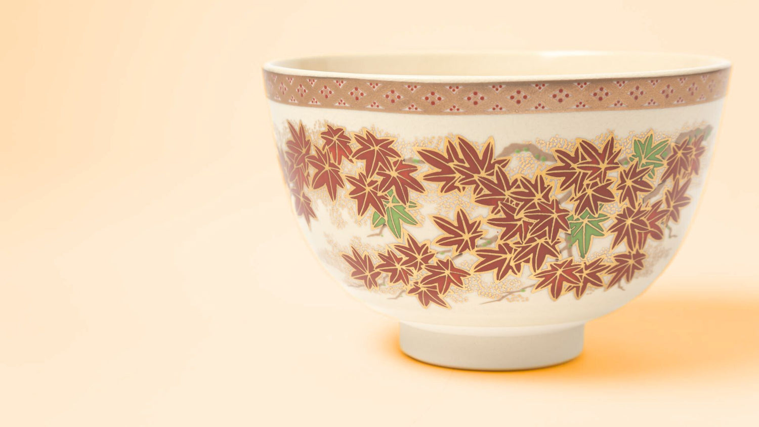 Japanese ceramic Matcha bowl adorned with autumn maple leaves in red and green, accented with gold details.