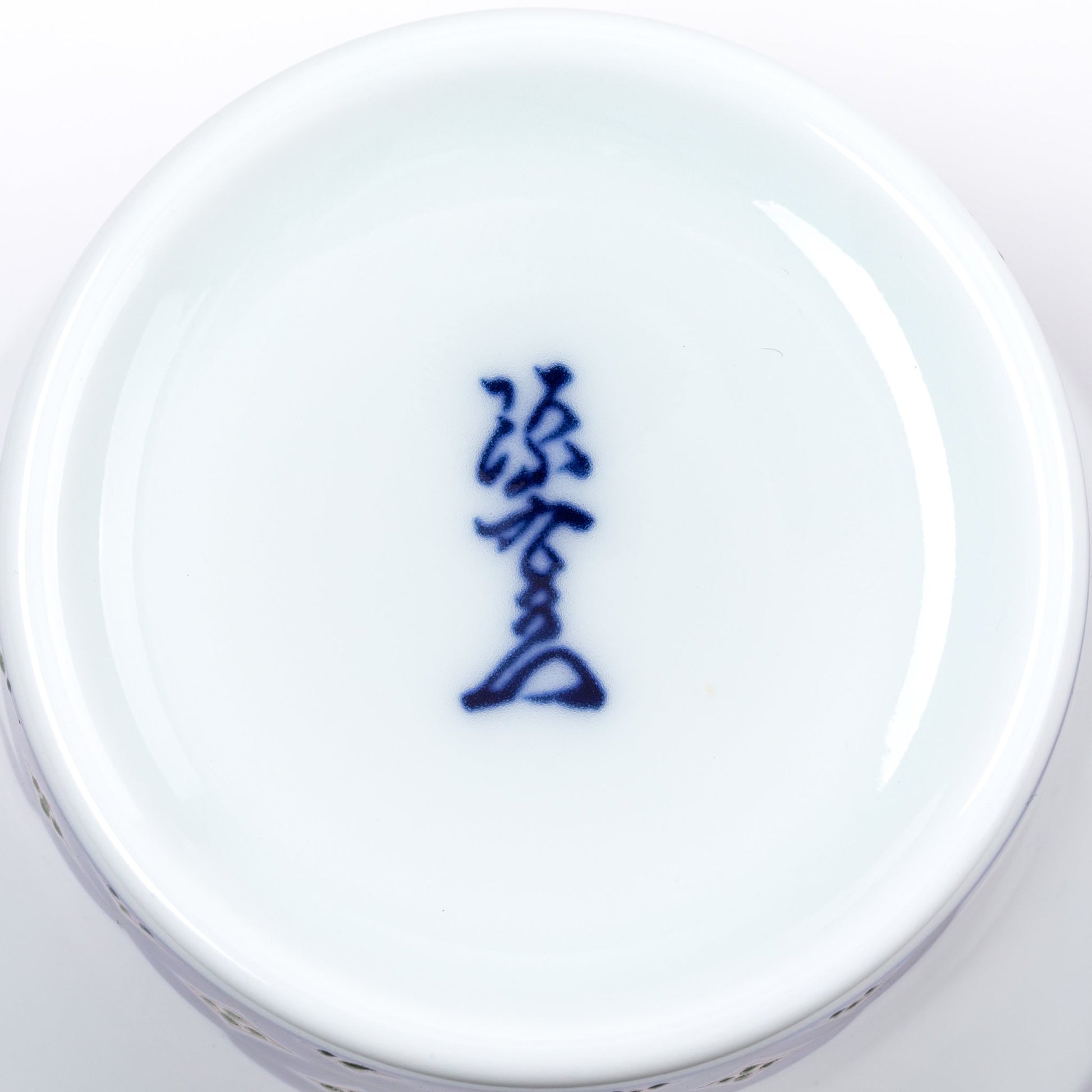 Close-up view of the bottom of a porcelain cup, featuring a blue kanji mark on a smooth white base, representing the Gen-emon kiln, known for its traditional Japanese craftsmanship.