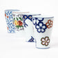 A set of four porcelain cups from the Gen-emon kiln, each showcasing unique hand-painted designs. The nearest cup features a scattered flower motif in vibrant colors, while the others display intricate patterns and fruit-inspired designs, all highlighting traditional Japanese craftsmanship.