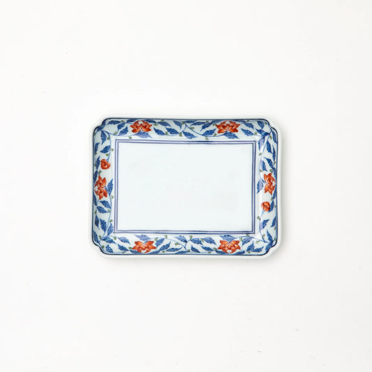 A Gen-emon Kiln Arita porcelain rectangle plate photographed from above, with a white center field framed by a thin cobalt line and a hand painted border of cobalt blue karakusa vines with iron red flowers and green accents, with clipped corners, against a white background.