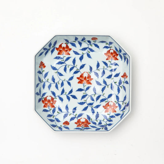 A Gen-emon Kiln Arita porcelain square plate photographed from above, with a white ground and hand painted cobalt blue karakusa vine motif with iron red flowers and green leaf accents filling the interior, and a thin cobalt rim border, against a white background.