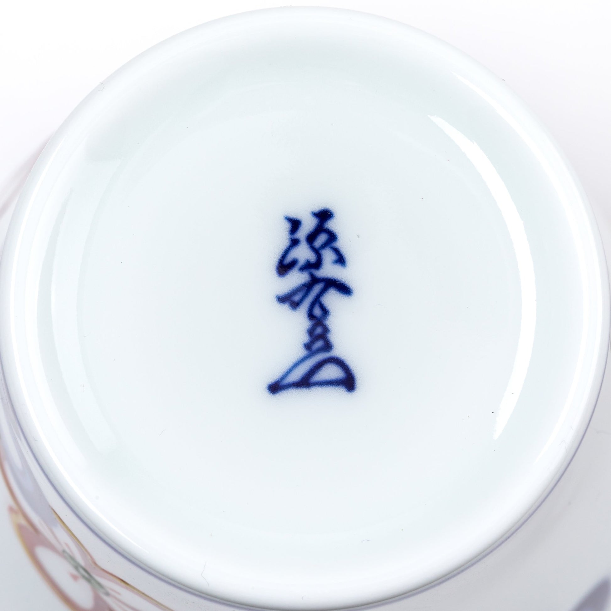 Close-up view of the bottom of a porcelain cup, featuring a blue kanji mark on a smooth white base, representing the Gen-emon kiln, known for its traditional Japanese craftsmanship.