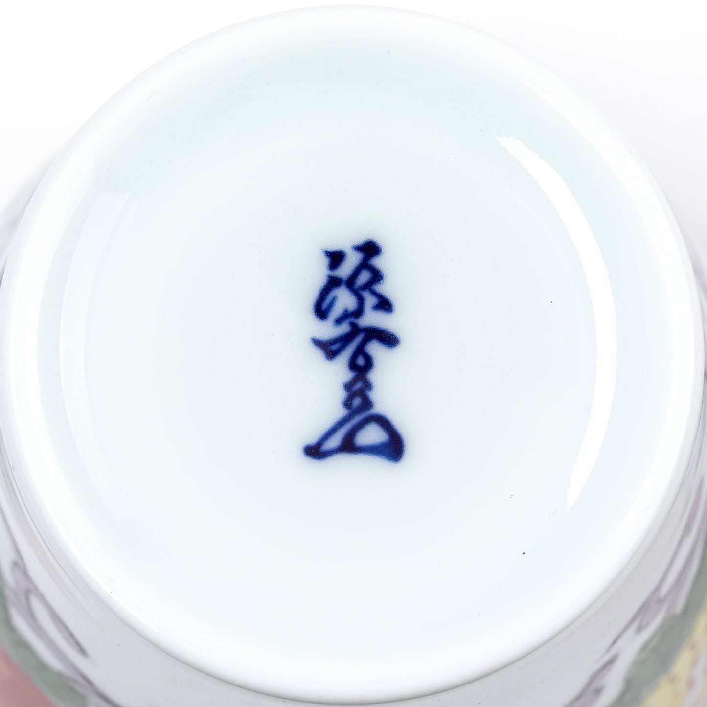 Close-up view of the bottom of a porcelain cup, featuring the blue kanji mark from the Gen-emon kiln, a symbol of traditional Japanese craftsmanship.