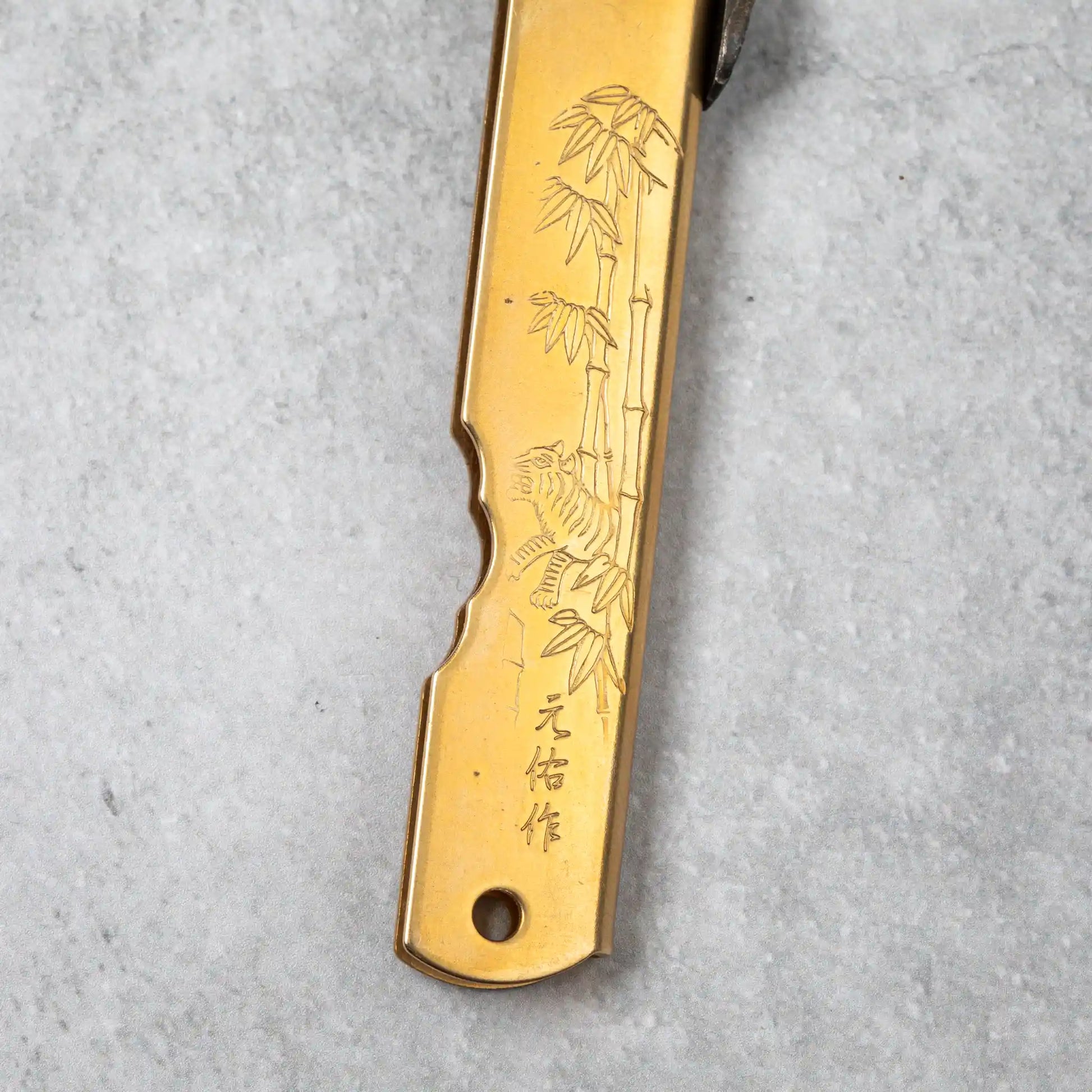 Back side of the Higonokami Damascus knife handle with an engraving of bamboo and a tiger, symbolizing strength and resilience.