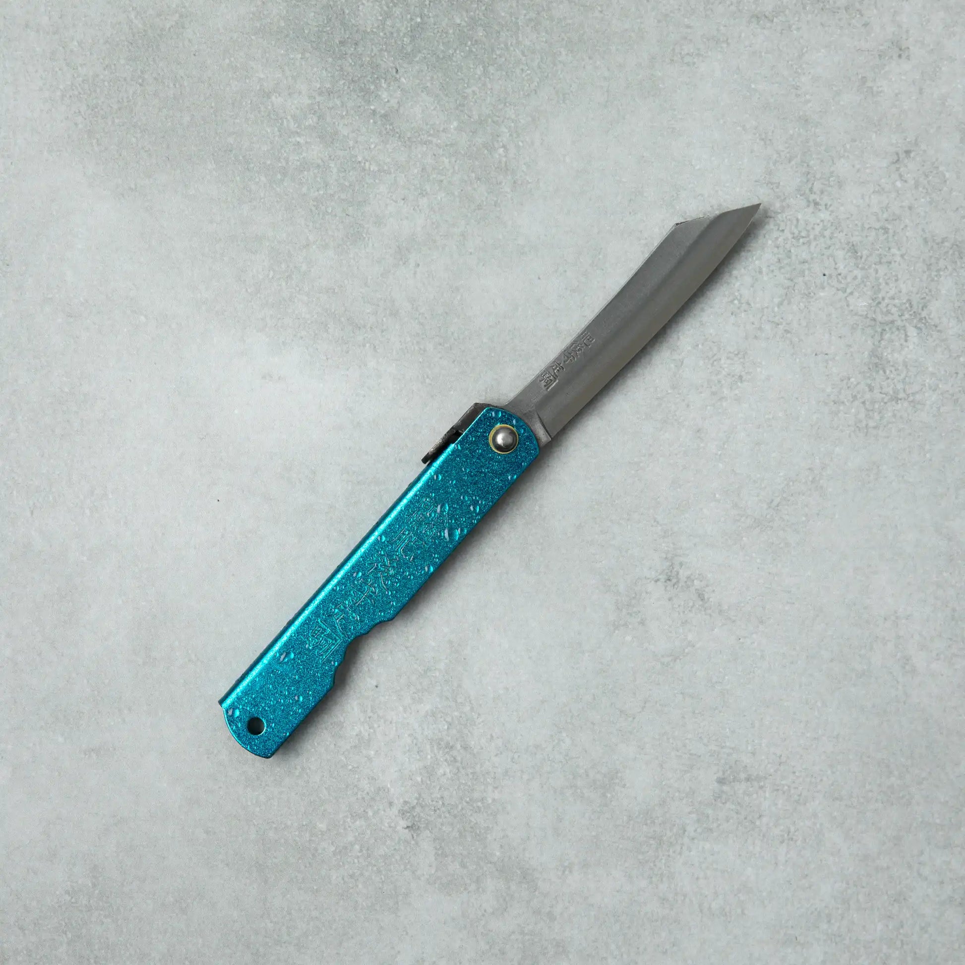 Full view of a Higonokami knife laid on a flat surface, showcasing its metallic blue handle and long blade with clean lines.