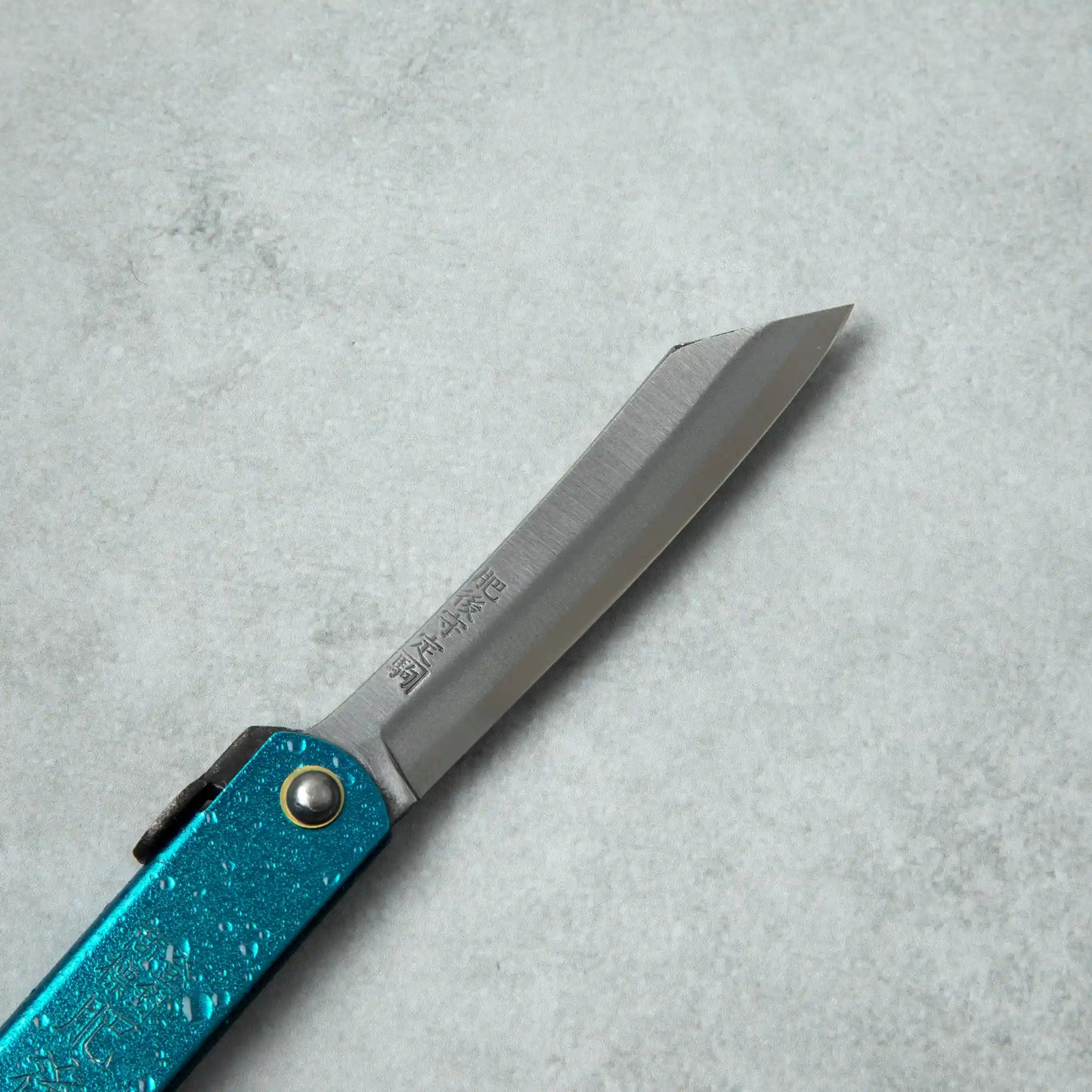 Close-up side view of the blade of a Higonokami knife, featuring a sleek, curved design with visible engravings near the handle.