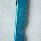 Close-up of the metallic blue handle of a Higonokami knife, displaying engraved Japanese characters with water droplets on the surface.