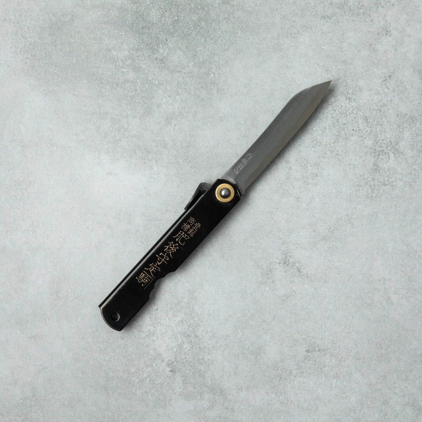 Full view of the Higonokami White Steel Bamboo knife with a black handle and a long, pointed blade, laid flat on a gray surface.