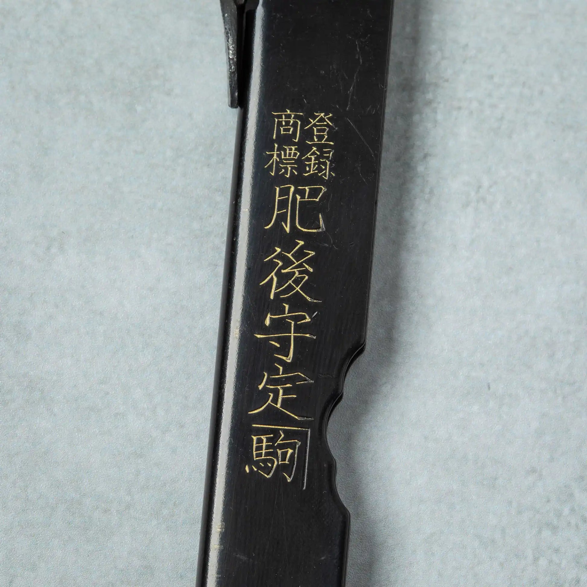 Detailed view of the engraved golden Japanese characters on the black handle of the Higonokami White Steel Bamboo knife.