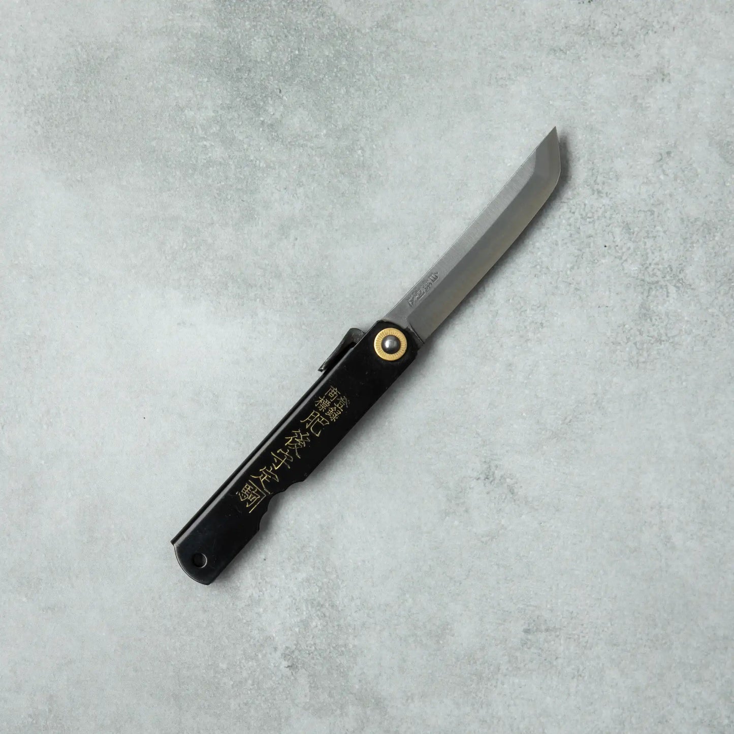 Full view of the Higonokami White Steel Sword knife with a black handle and sleek blade, laid flat on a gray surface.