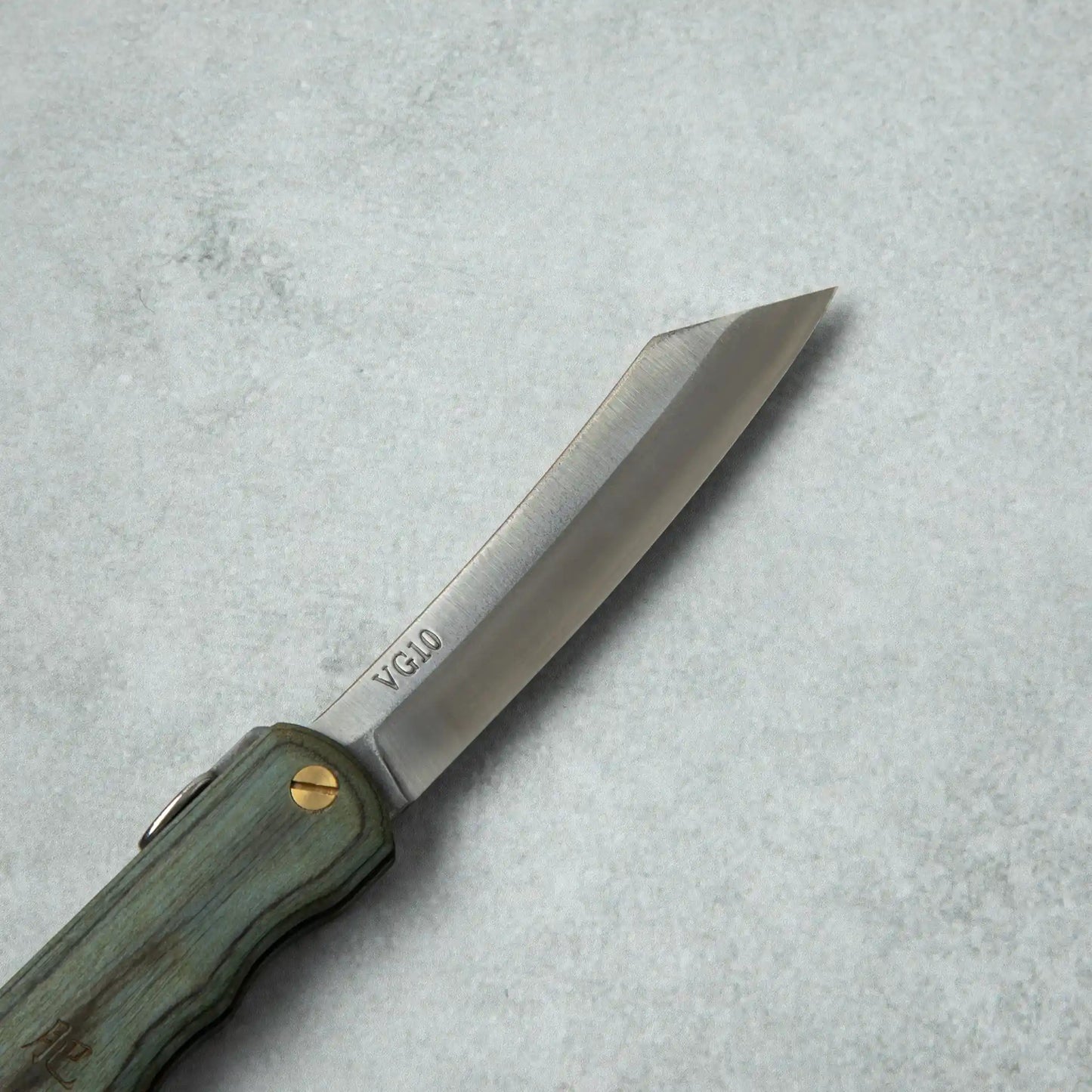 Side view of the Higonokami Woody VG10 knife blade, showing its sharp edge with VG10 marking, and a brass screw pivot on the Blue wooden handle.