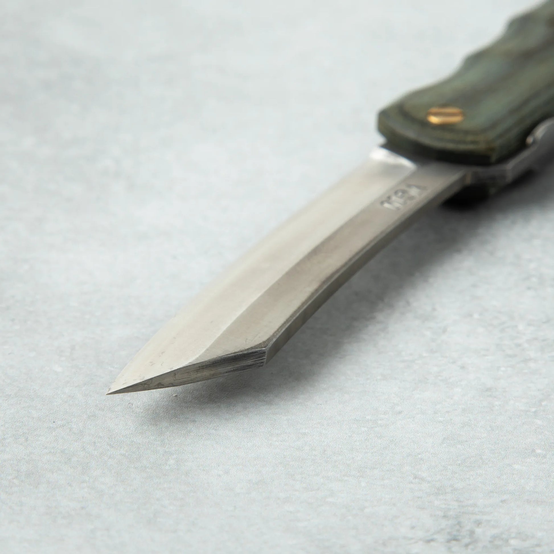 Close-up of the tip of the Higonokami Woody VG10 knife, showcasing the sharp, angular blade with a smooth finish.