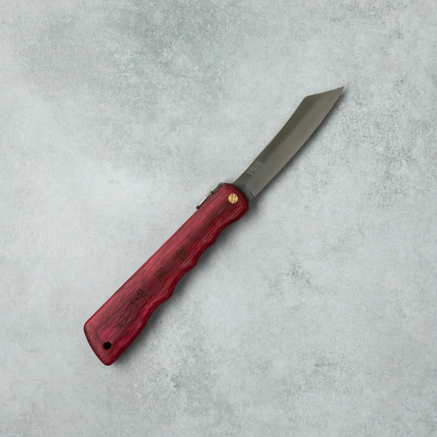 Full view of the Higonokami Woody VG10 knife with a red wooden handle and sleek, sharp blade, laid flat on a gray surface.