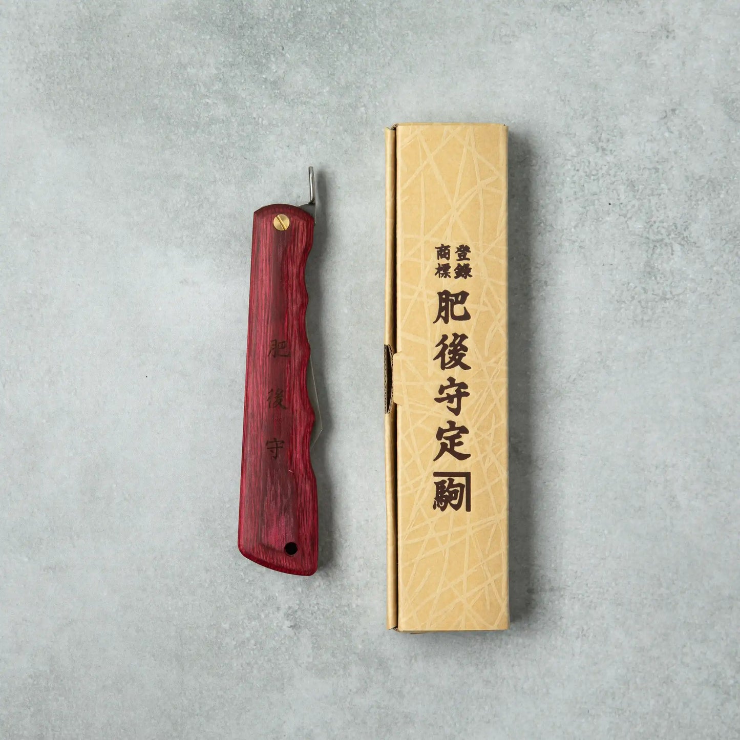 Higonokami Woody VG10 knife with a red wooden handle, displayed next to its traditional cardboard packaging featuring Japanese characters.