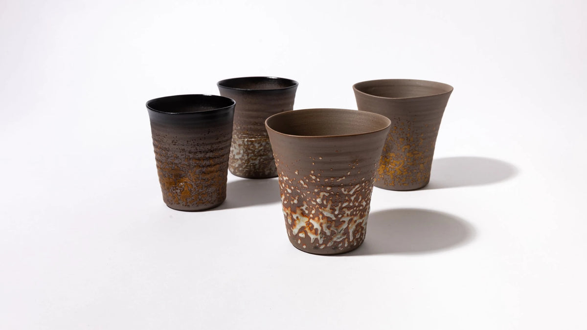 Four handmade ceramic cups with textured, ribbed bodies and organic rust-orange glaze variations, arranged on a clean white studio background.