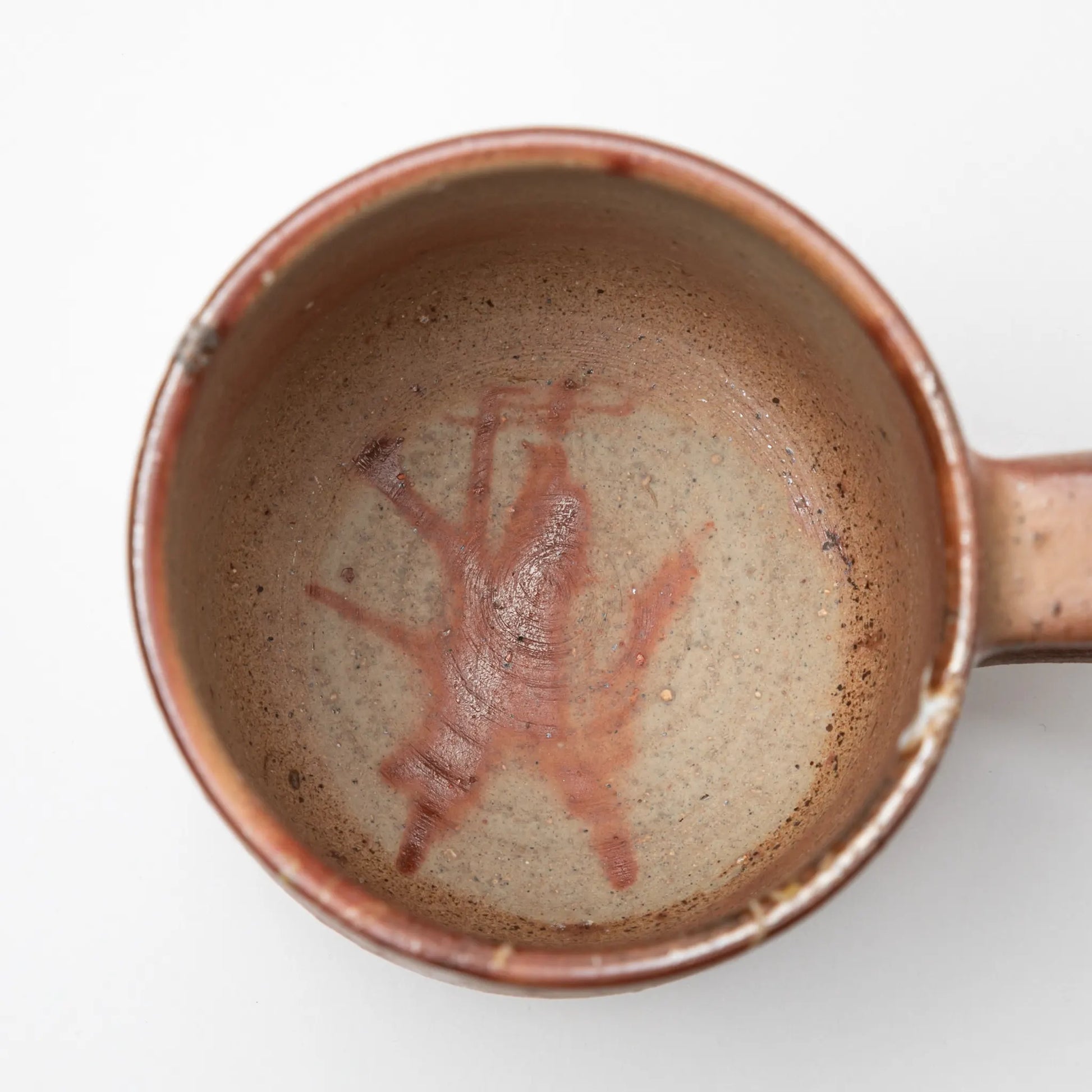 A Hozan Kiln Hidasuki Mug viewed from above, showcasing a subtle reddish abstract pattern against a beige clay surface.