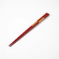 Pair of red lacquered chopsticks with gold detailing, highlighting their minimalist yet elegant design.