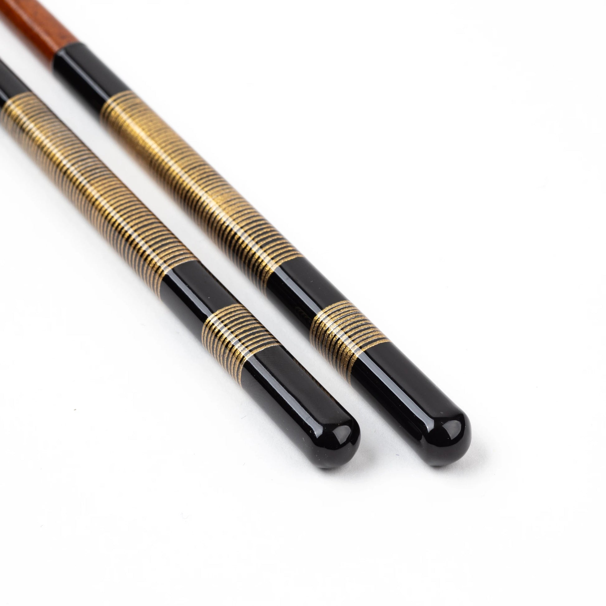 Close-up of lacquered chopsticks with gold and black striped accents, highlighting the artisanal craftsmanship.