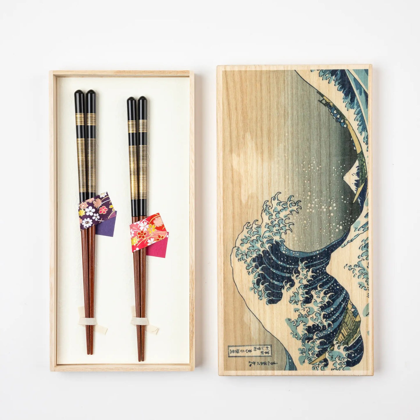 A pair of Japanese chopsticks with gold and black details in a paulownia box featuring Katsushika Hokusai's "The Great Wave."