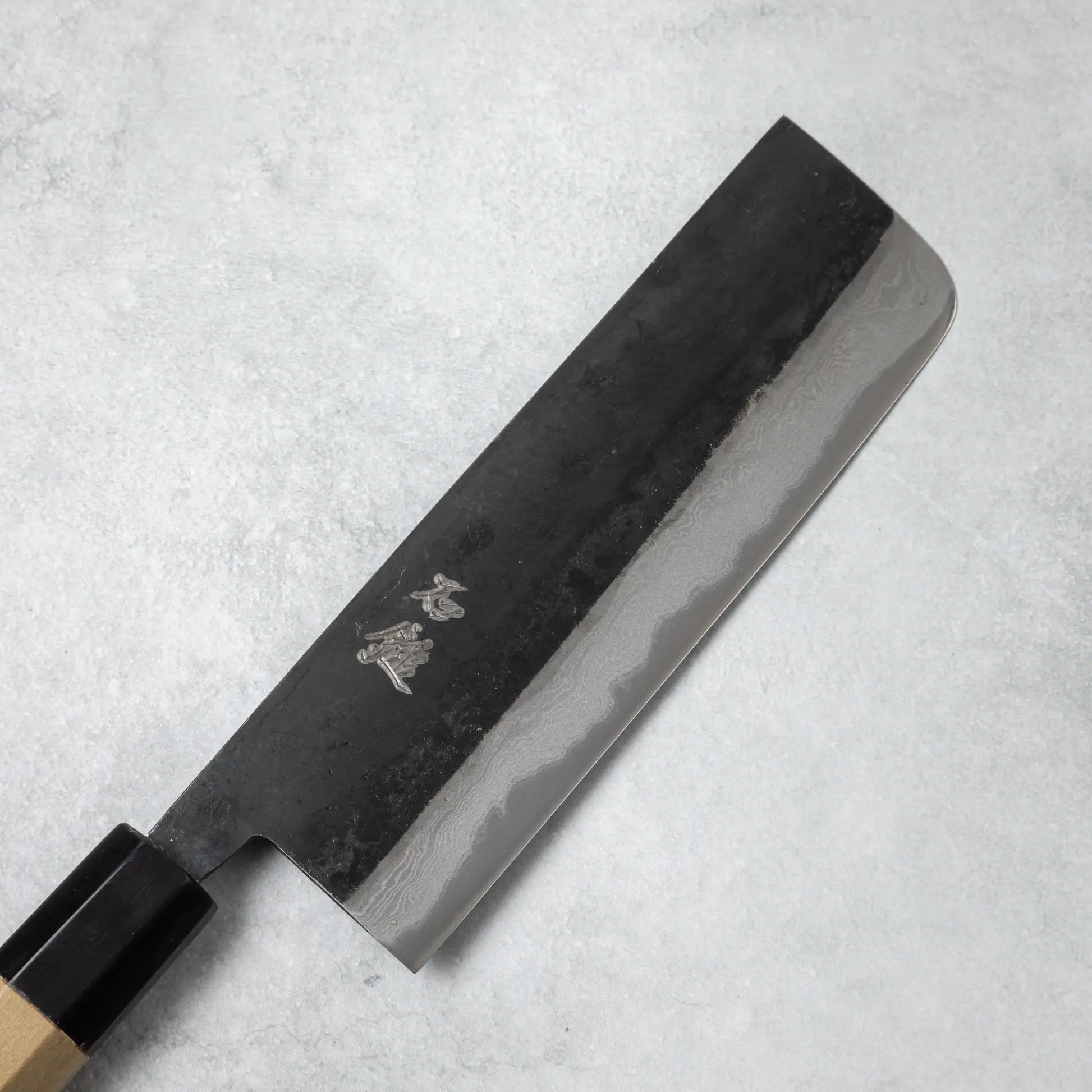 Close-up of the Ishizuchi Blue Steel No.2 Nakiri Damascus Knife blade, showcasing the beautiful wave-like Damascus pattern and engraved kanji.