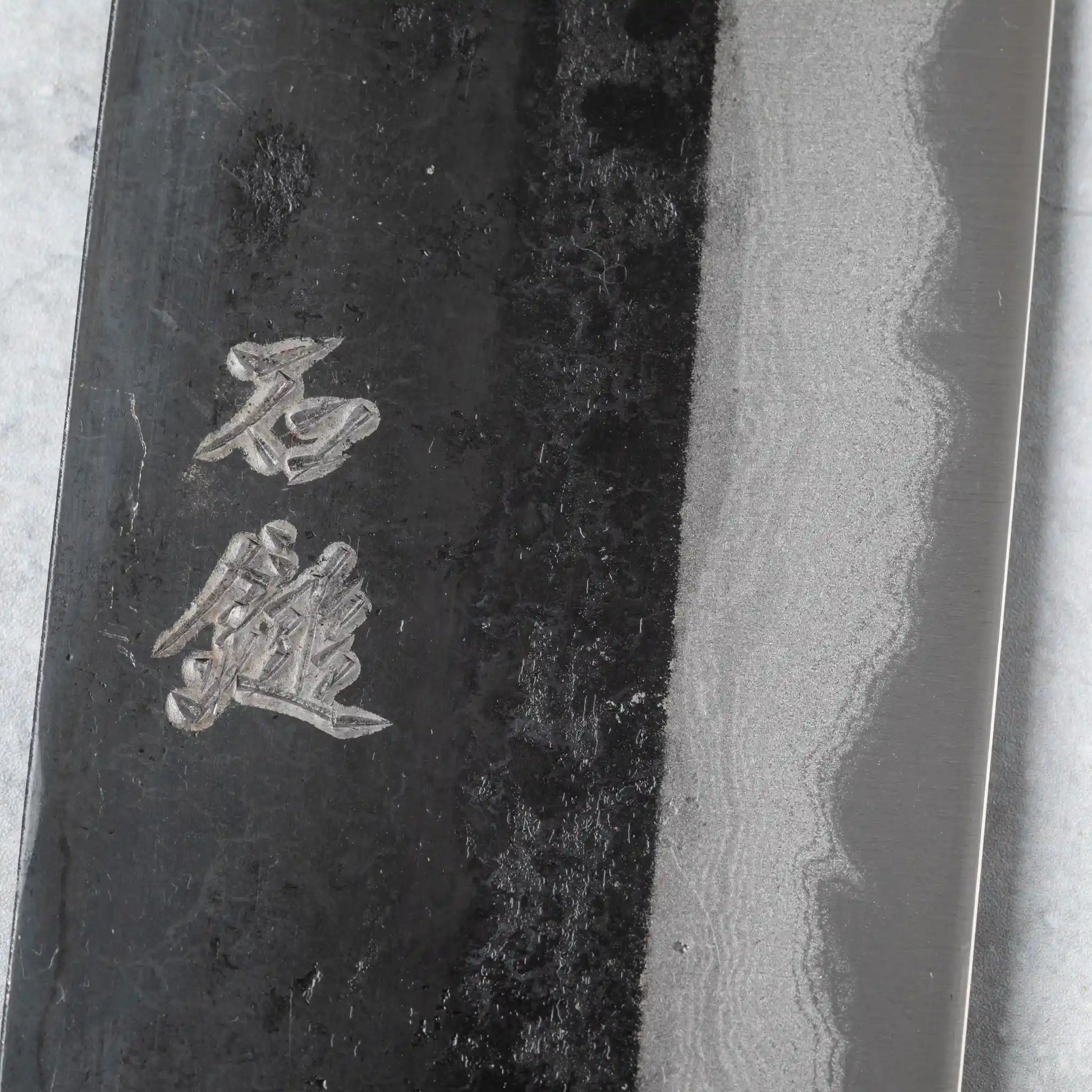 Close-up of kanji engraving on the Damascus-patterned blade of the Ishizuchi Blue Steel No.2 Nakiri Knife, highlighting the intricate detail and traditional craftsmanship.