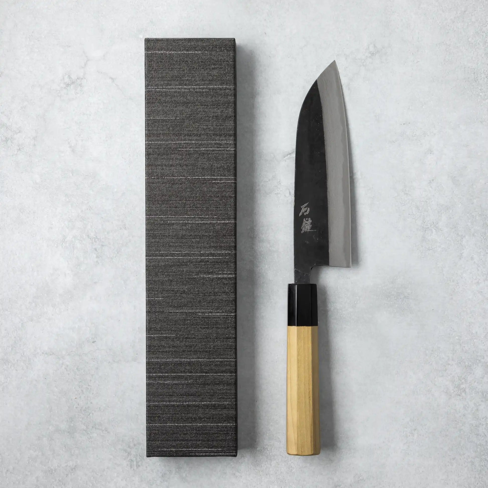 Ishizuchi Blue Steel No.2 Santoku Damascus Knife with magnolia handle, displayed next to a minimalist black box, presenting a refined Japanese aesthetic.