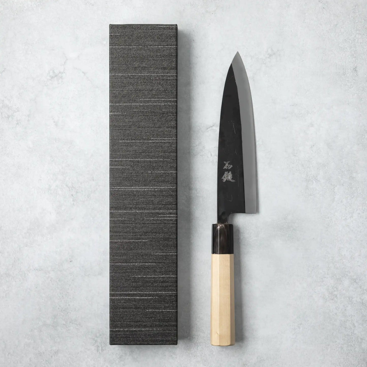 Ishizuchi Blue Steel No.2 Chef Knife with magnolia handle displayed next to a minimalist black box on a light background.