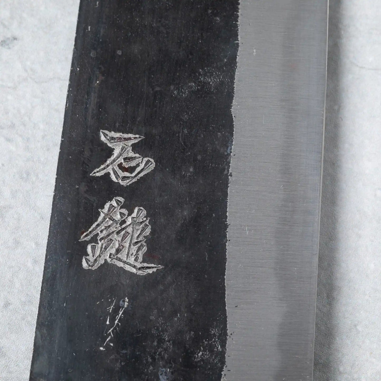 Close-up of the kanji engraving on the Ishizuchi Blue Steel No.2 Kiritsuke Knife blade, capturing the intricate details of Japanese artistry.