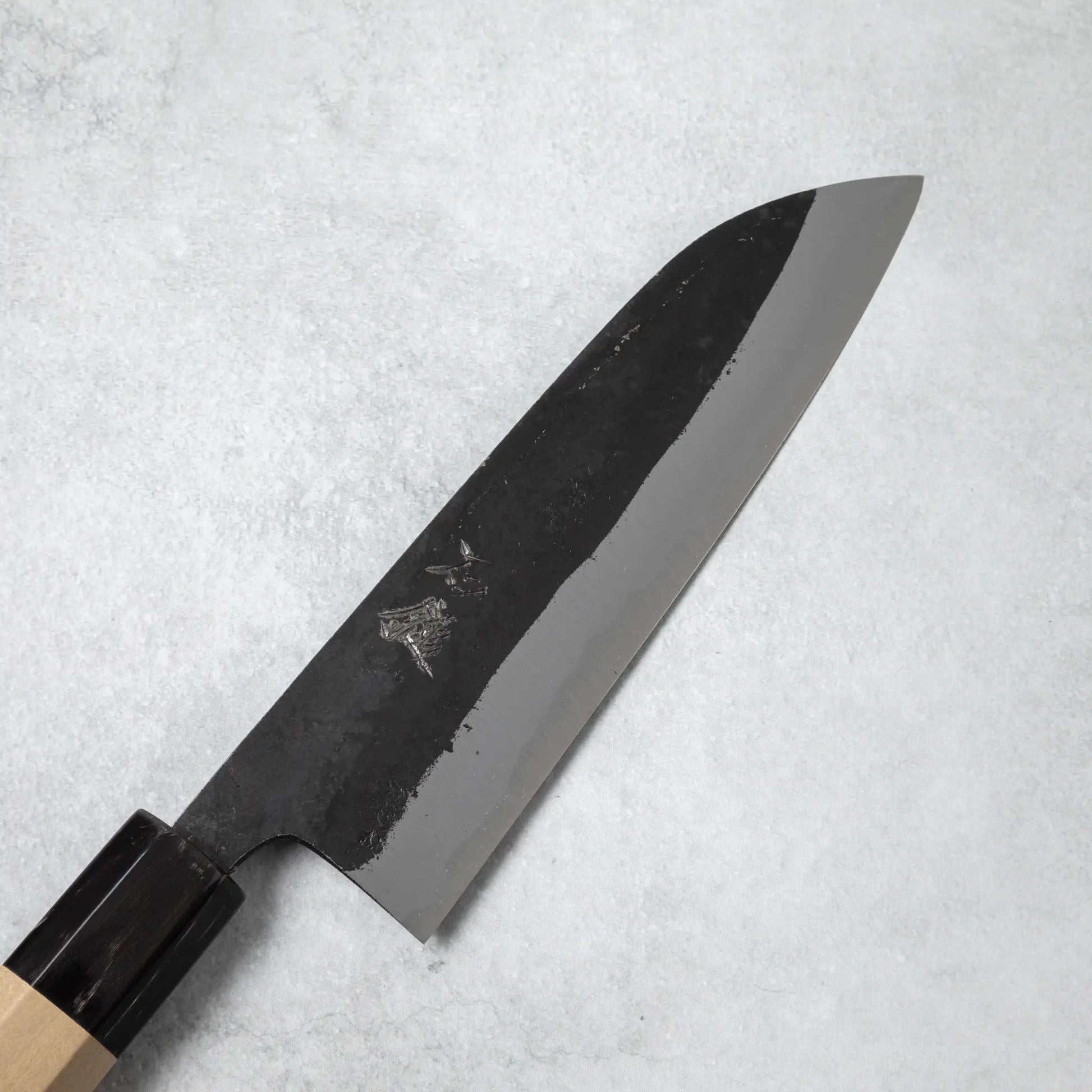 Close-up of the blade on the Ishizuchi Blue Steel No.2 Santoku Knife with engraved kanji characters, highlighting its sharpness and traditional finish.