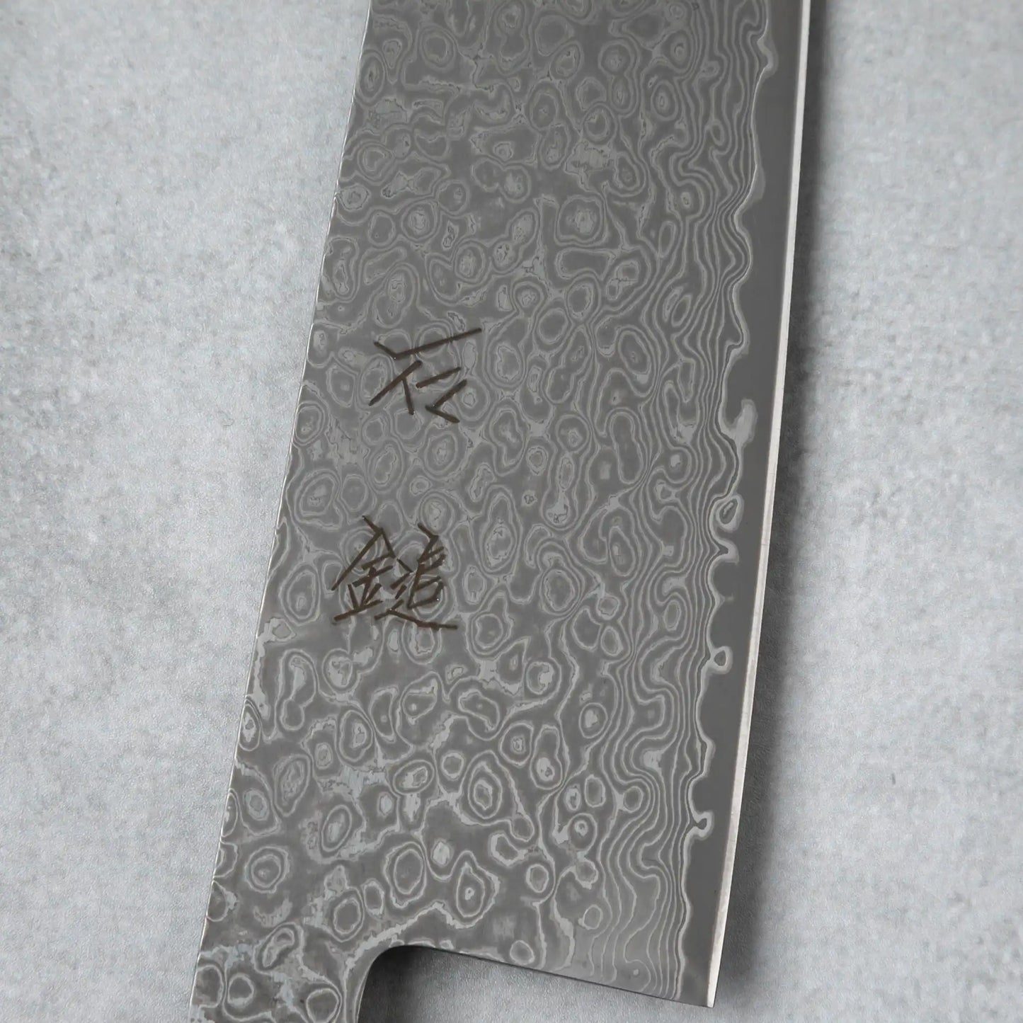 Focused shot of the kanji engraving on the Damascus blade of the Ishizuchi VG10 Chef Knife, emphasizing its craftsmanship and attention to detail.