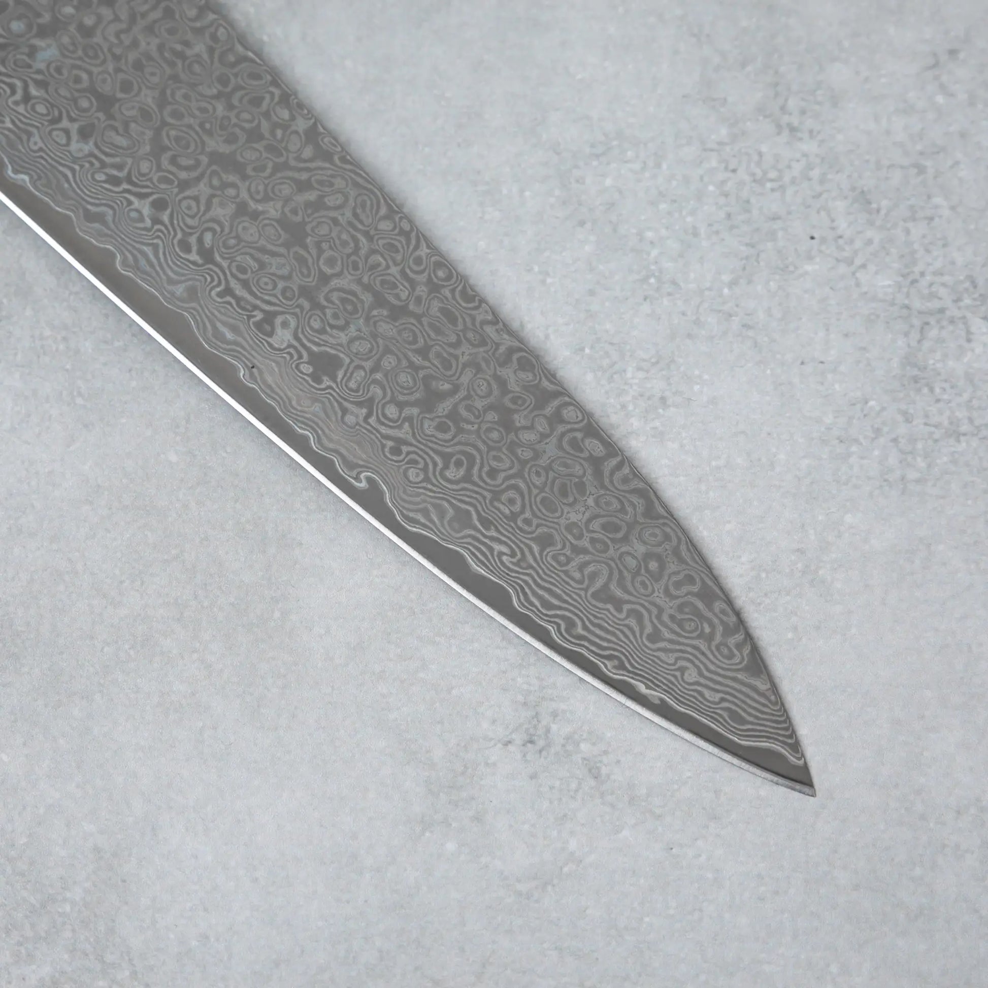 Zoomed-in view of the sharp tip of the Ishizuchi VG10 Damascus Chef Knife, highlighting the intricate Damascus steel design.