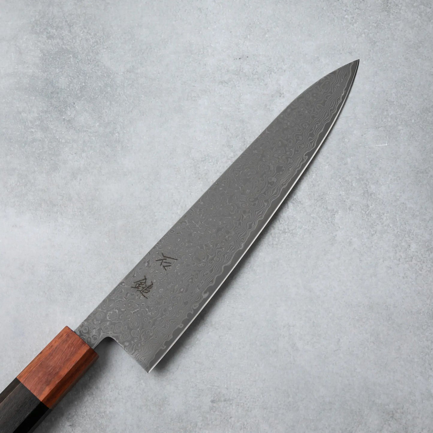 Close-up of the Damascus steel blade on the Ishizuchi VG10 Chef Knife, showcasing its elegant wave-like patterns and engraved kanji characters.