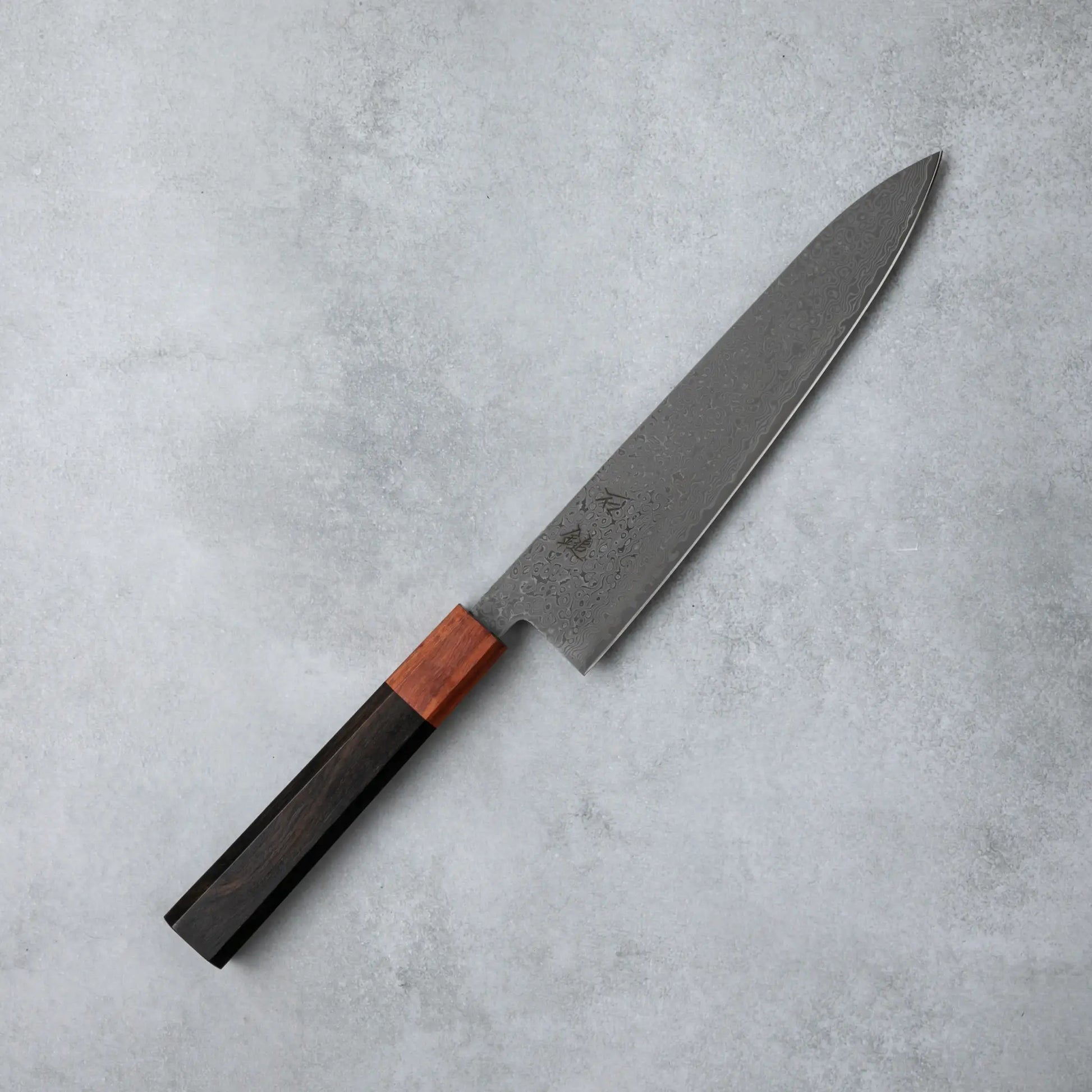 Full view of the Ishizuchi VG10 Damascus Chef Knife with its intricate Damascus steel blade and ebony wood handle, placed on a minimalist gray background.