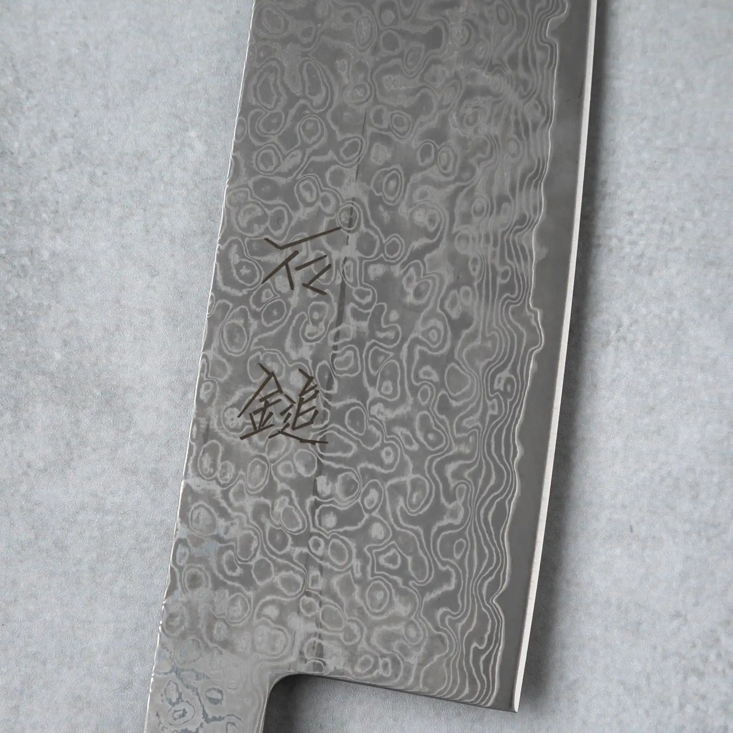 Focused shot of the kanji engraving on the Damascus blade of the Ishizuchi VG10 Kiritsuke Knife, illustrating its intricate detailing and superior craftsmanship.