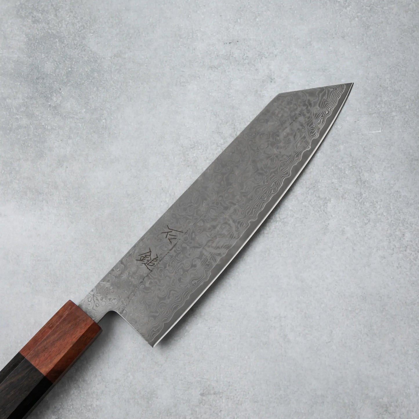 Close-up of the Damascus steel blade on the Ishizuchi VG10 Kiritsuke Knife, featuring intricate wave-like patterns and engraved kanji characters.