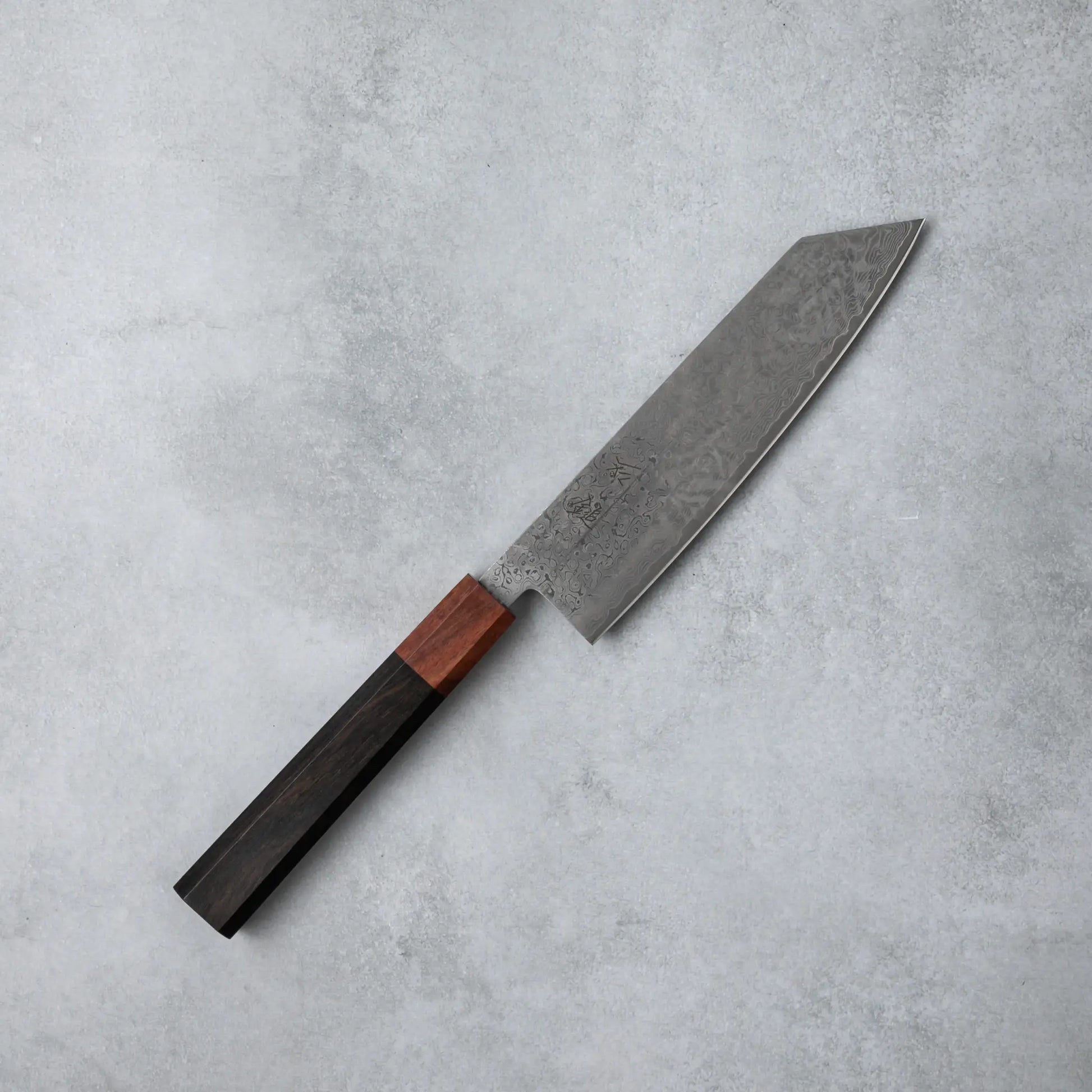 Full view of the Ishizuchi VG10 Damascus Kiritsuke Knife, showcasing its distinctive straight-edged blade and ebony wood handle, set against a soft gray background.