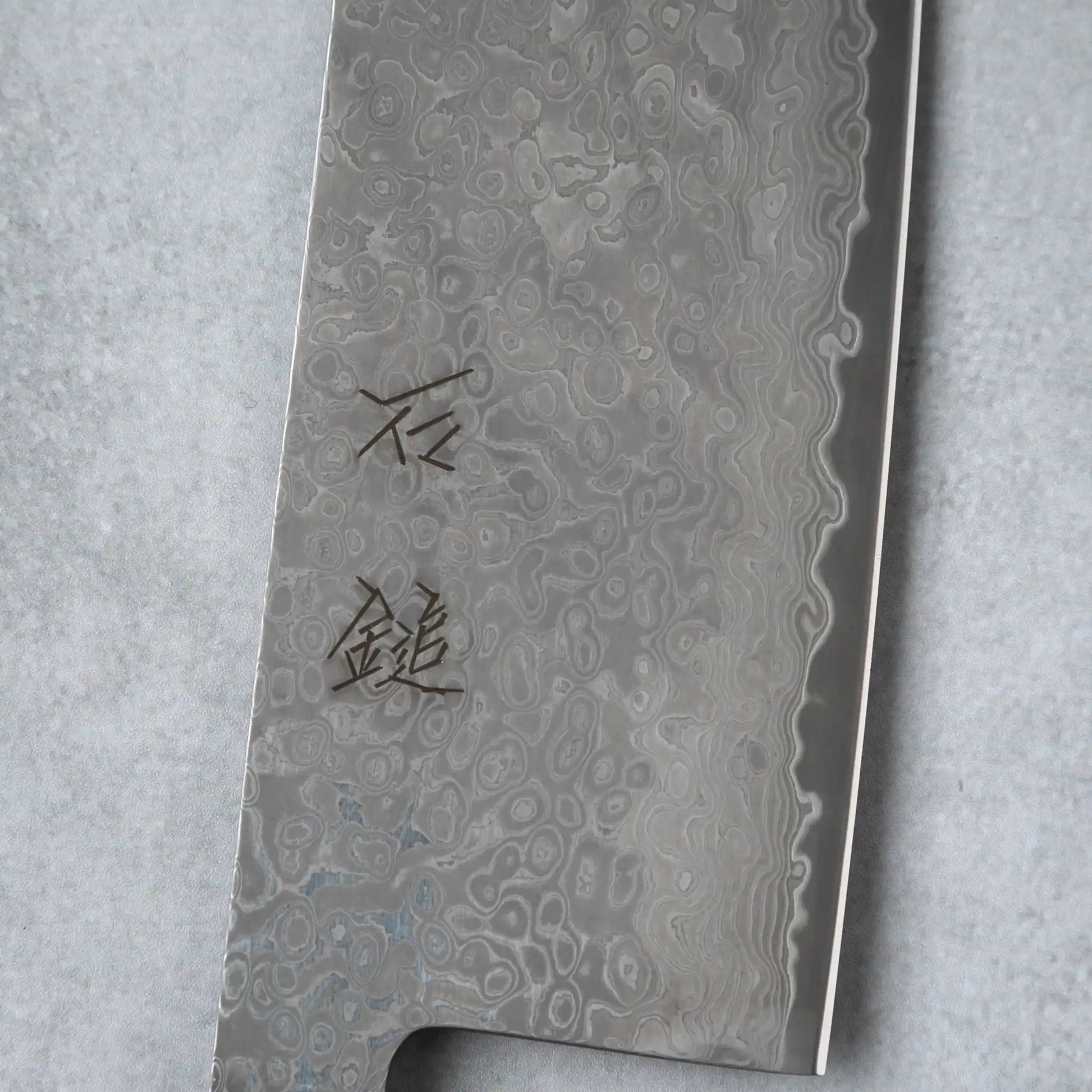 Focused shot of the kanji engraving on the blade of the Ishizuchi VG10 Nakiri Knife, demonstrating the craftsmanship and detail in the Damascus steel.