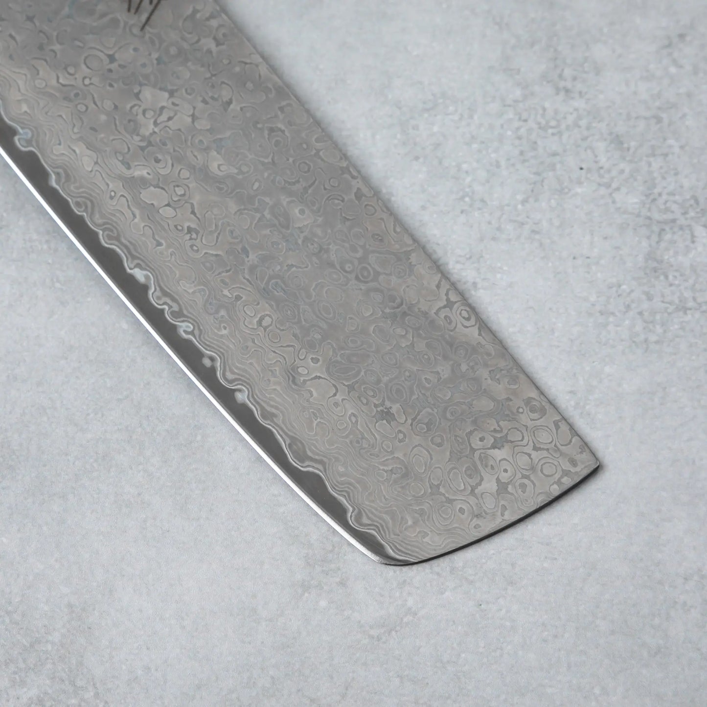 Zoomed-in view of the sharp edge and tip of the Ishizuchi VG10 Damascus Nakiri Knife, emphasizing the blade's precision and exquisite Damascus steel pattern.