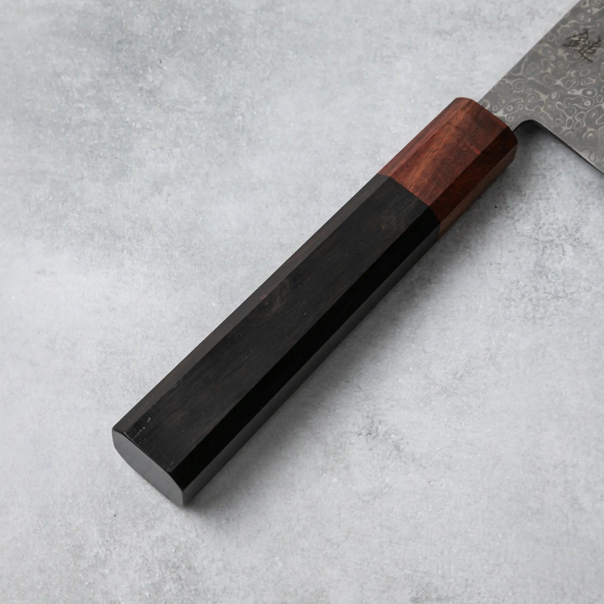 Detailed view of the Ishizuchi VG10 Damascus Nakiri Knife's ebony wood handle with a rosewood accent, highlighting its sleek and ergonomic design.