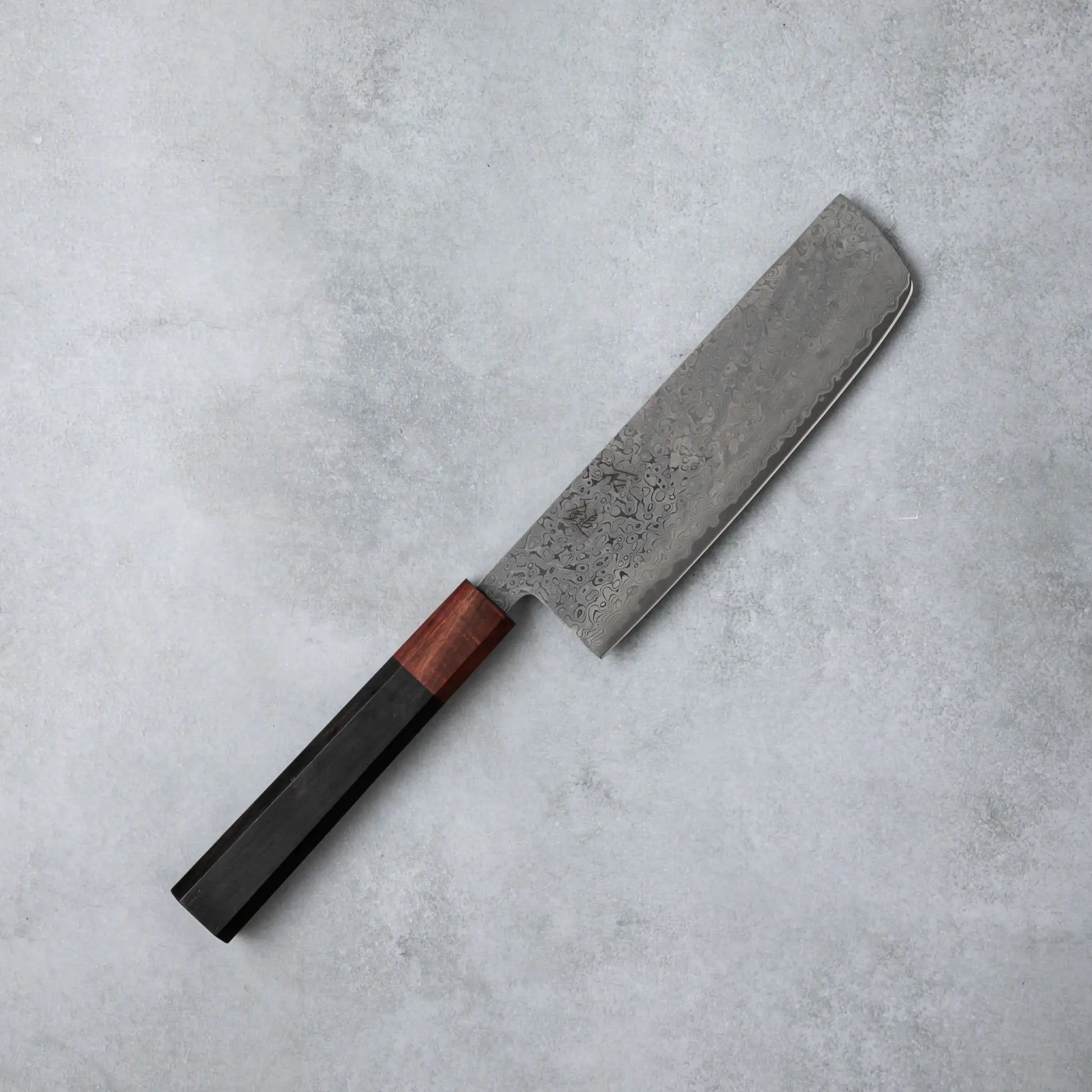 Full view of the Ishizuchi VG10 Damascus Nakiri Knife, featuring a rectangular blade and polished ebony wood handle, set against a simple gray surface.