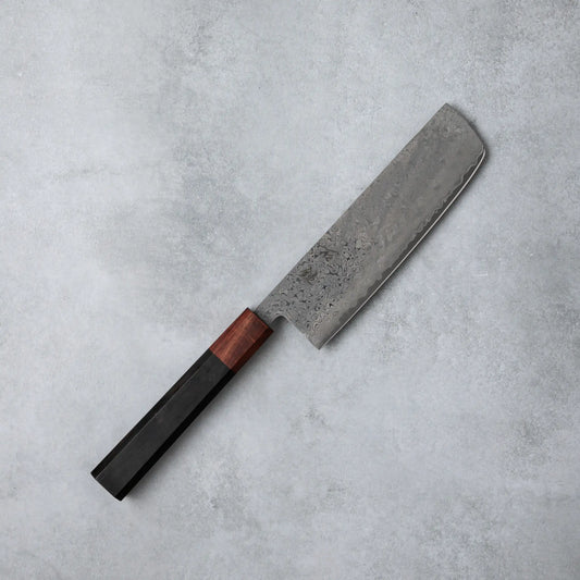 Full view of the Ishizuchi VG10 Damascus Nakiri Knife, featuring a rectangular blade and polished ebony wood handle, set against a simple gray surface.