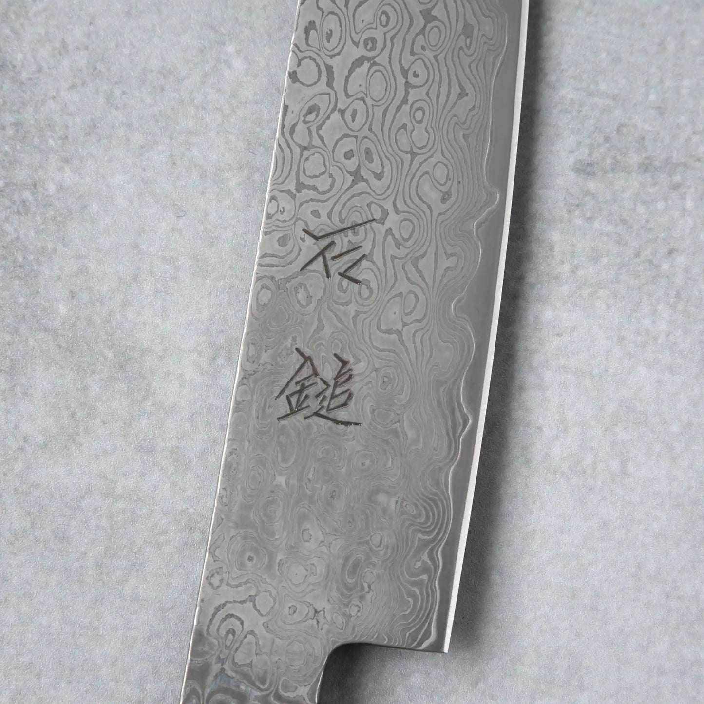 Focused shot of the kanji engraving on the Damascus blade of the Ishizuchi VG10 Petty Knife, showcasing the artistry and detail in its craftsmanship.