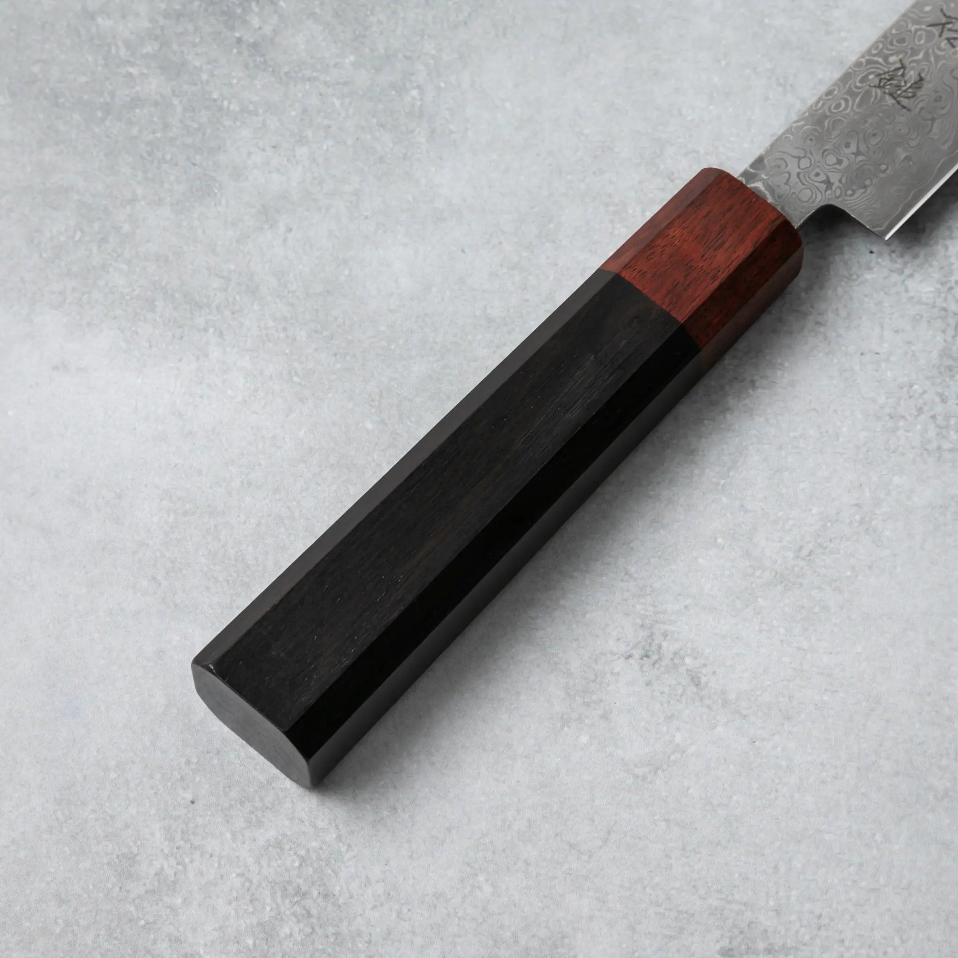 Detailed view of the Ishizuchi VG10 Damascus Petty Knife's ebony wood handle with a rosewood accent, highlighting its smooth finish and ergonomic design.