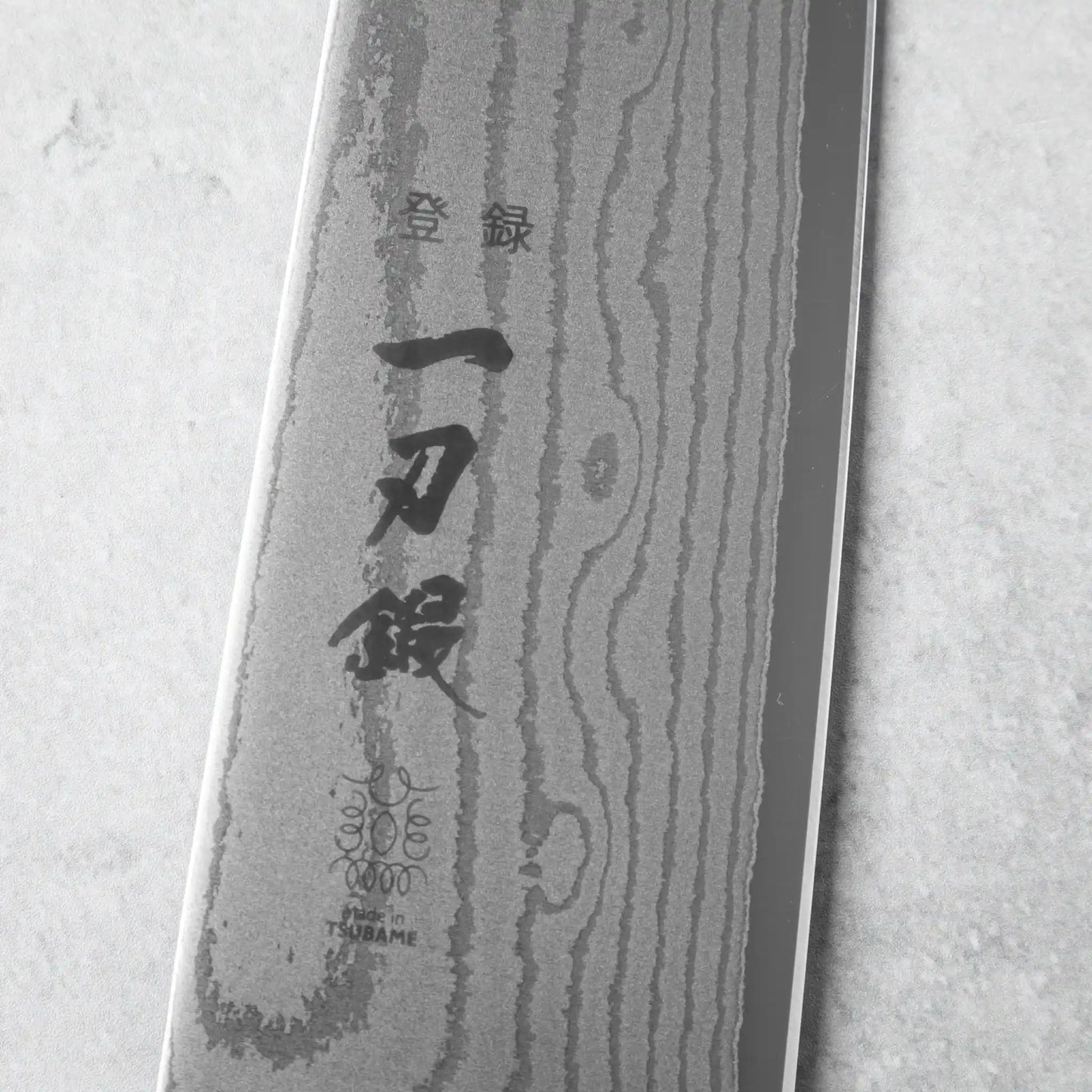 The tip of the chef’s knife, showcasing the fine tapering and polished Damascus layers.